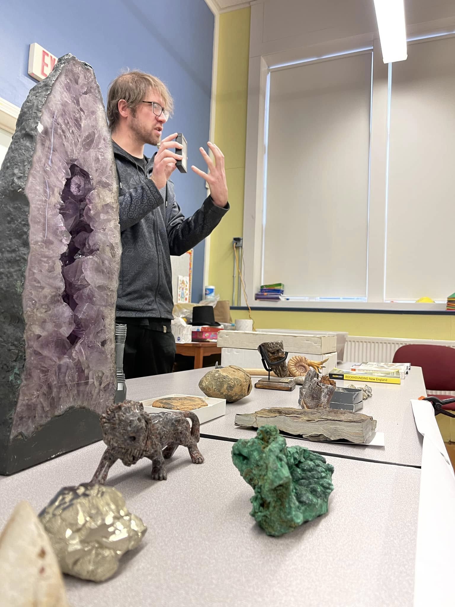 Louis Fazzina speaking beside a table of minerals and fossils at Pinecroft School